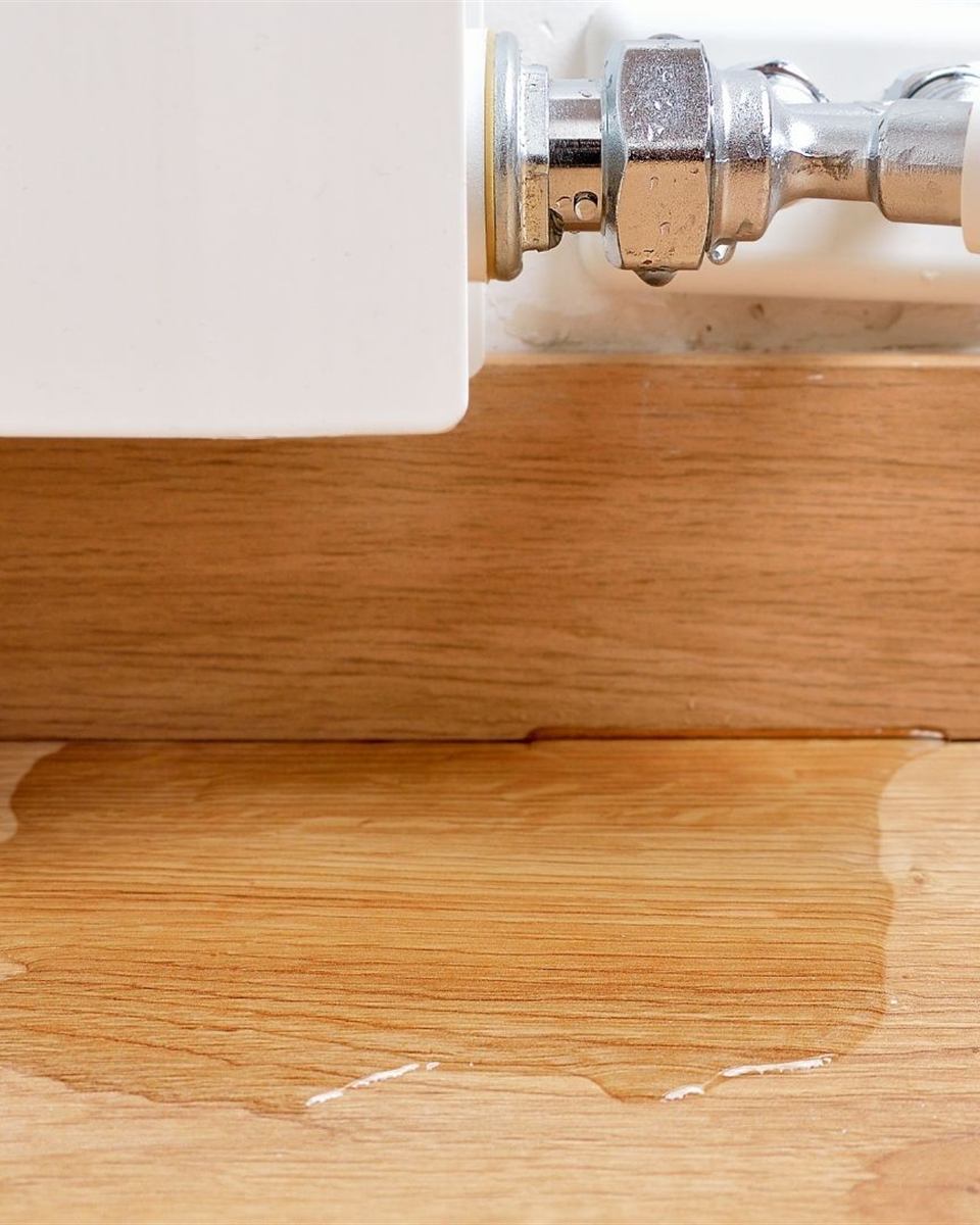 Water dripping from a corroded P-trap into a bowl under a bathroom sink